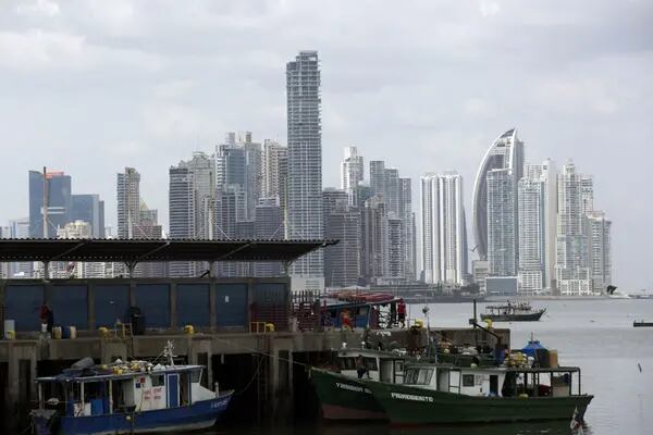 Fishermen sit at the dock beside the fish market as buildings stand in the skyline in the background in Panama City, Panama.