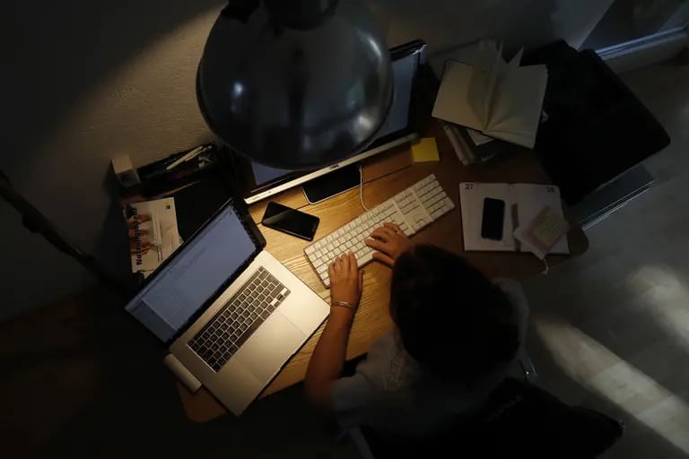 Una mujer trabaja con un ordenador de sobremesa junto a un portátil de Apple Inc. en una oficina doméstica por la noche.dfd
