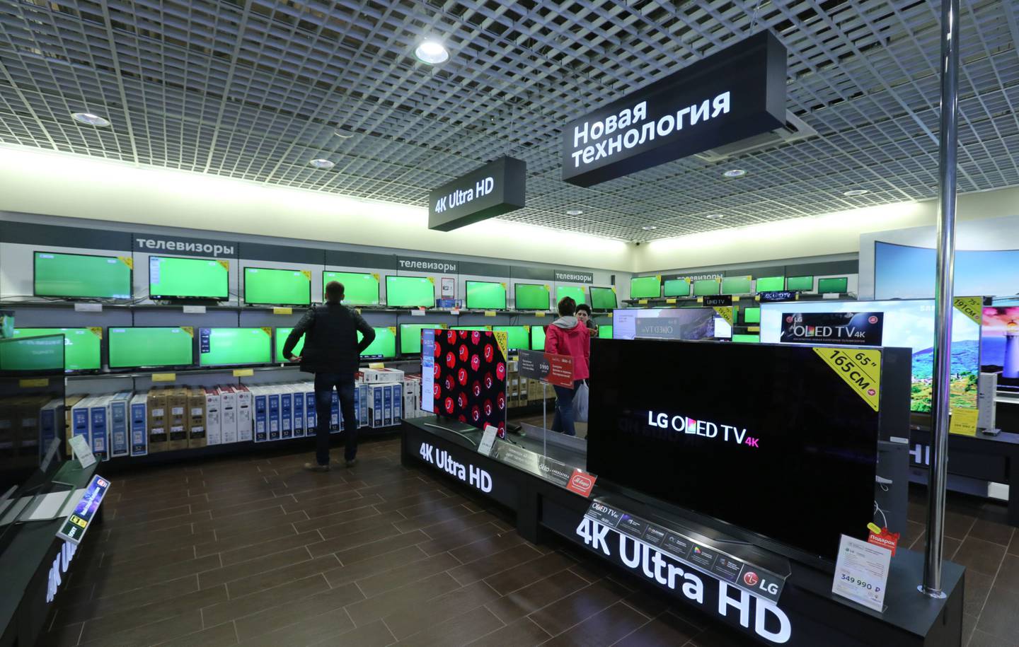 Customers browse digital television screens including a display of 4K ultra HD Oled products by LG Electronics Inc. inside an M.Video PJSC electronics store inside the Mega Khimki shopping mall in Khimki, Russia, on Sunday, April 23, 2017. M.Video operates a chain of consumer electronics and home appliances retail stores and is Russia's biggest electronics retailer. Photographer: Andrey Rudakov/Bloombergdfd