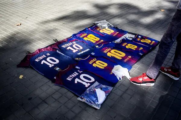Un vendedor callejero junto a camisetas de Lionel Messi y Neymar Jr.
