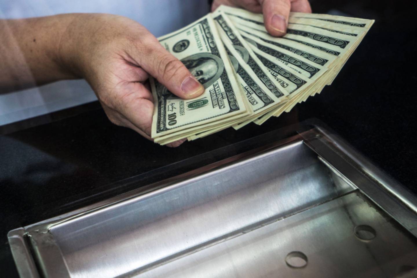 Un hombre sostiene billetes de cien dólares estadounidenses en una casa de cambio.