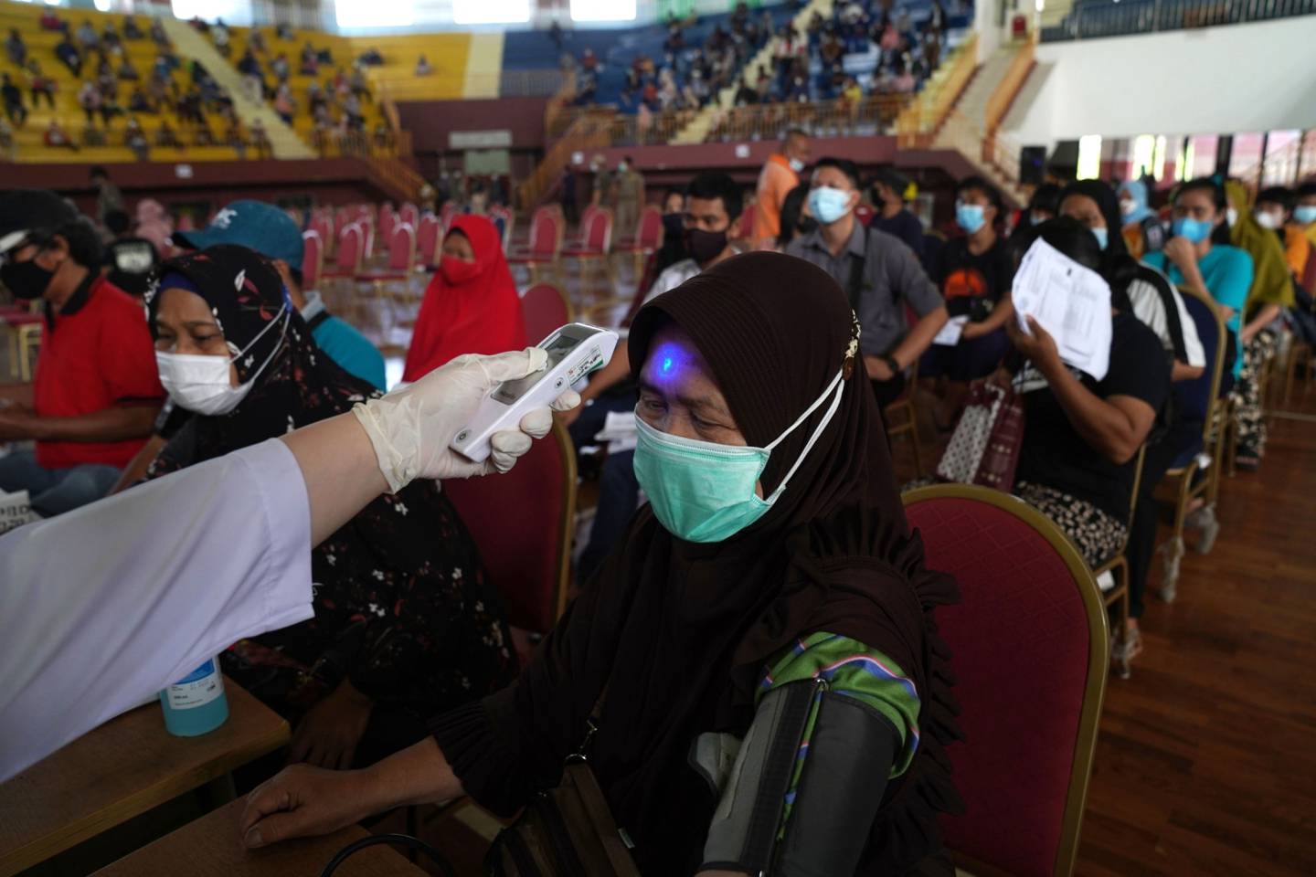 Una habitante de Indonesia espera mientras le toman su temperatura en un centro de vacunación en Jakarta.dfd