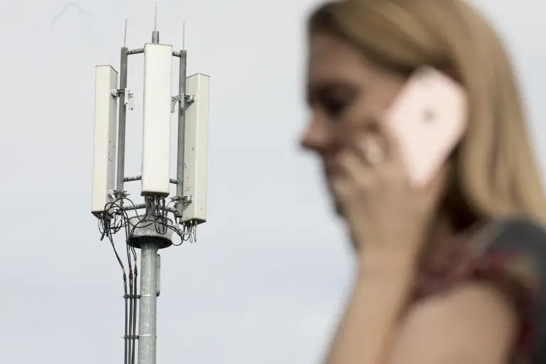 Un peatón utiliza un teléfono móvil a la vista de las antenas de un mástil de telecomunicaciones de telefonía móvil en esta fotografía arreglada en Shalford, Reino Unido, el lunes 13 de julio de 2020.dfd