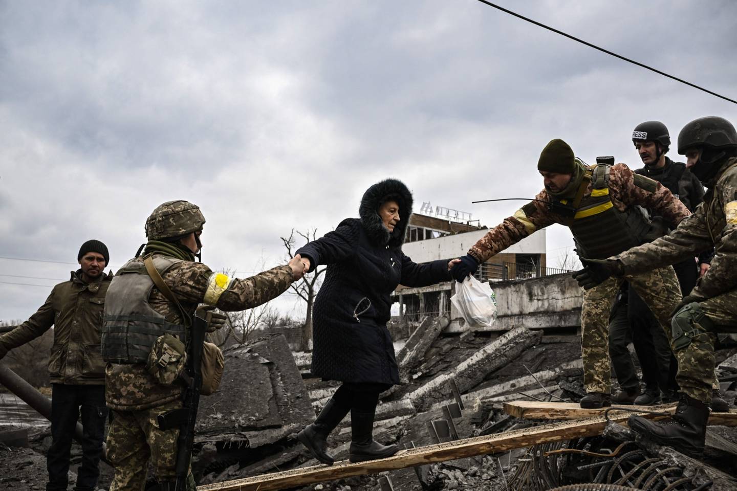 Una mujer recibe asistencia de fuerzas ucranianas para cruzar un puente destruido