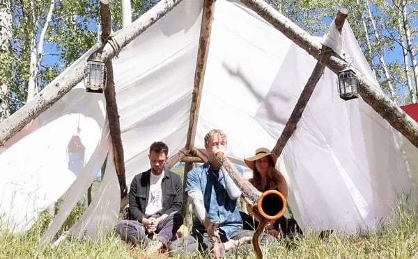 Três pessoas em uma tenda improvisada. Dois homens e uma mulher.