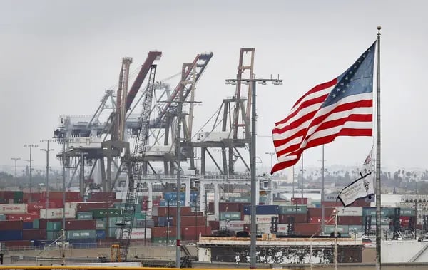 Una bandera de Estados Unidos ondea mientras grúas para descargar contenedores de transporte marítimo permanecen en el Puerto de Los Ángeles en San Pedro, California, Estados Unidos, el lunes 30 de junio de 2014.