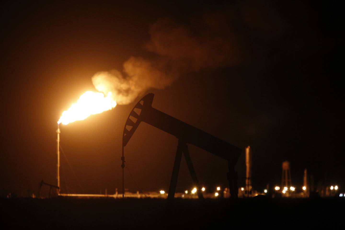 An oil pump jack near a flare at night. Photographer: Luke Sharrett/Bloomberg