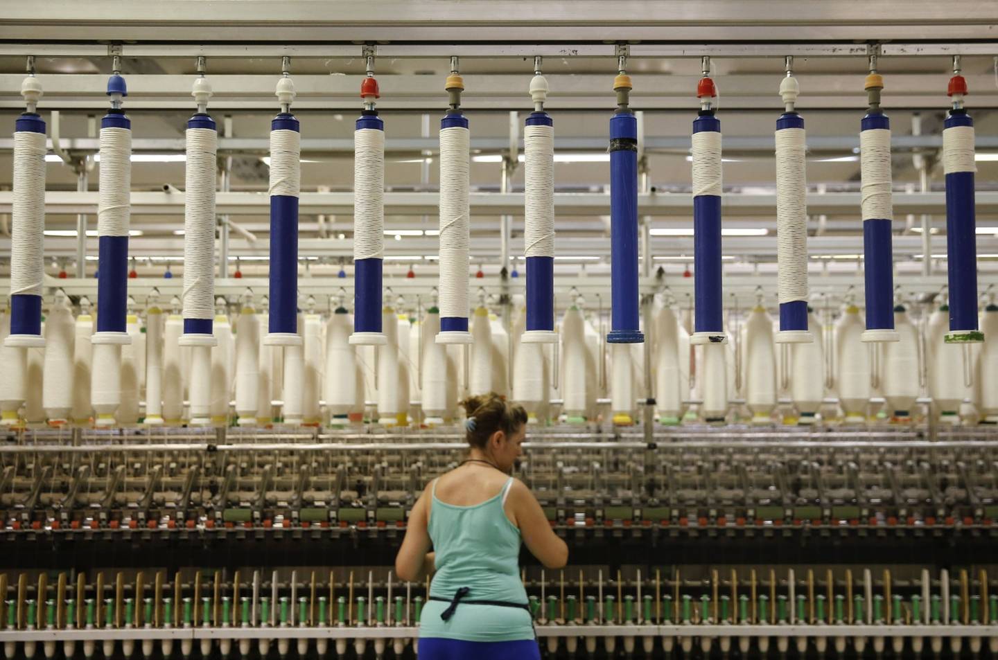 Los hilos de algodón cuelgan arriba mientras un empleado comprueba el hilado en la planta de procesamiento de Selected Textiles S.A. en Farsala, Grecia, el viernes 10 de julio de 2015.dfd