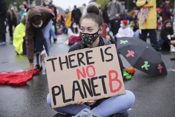 Mulher sentada na rua em protesto. Ela segura um cartaz escrito "There is no Planet B" (Não existe Planeta B, em tradução livre)