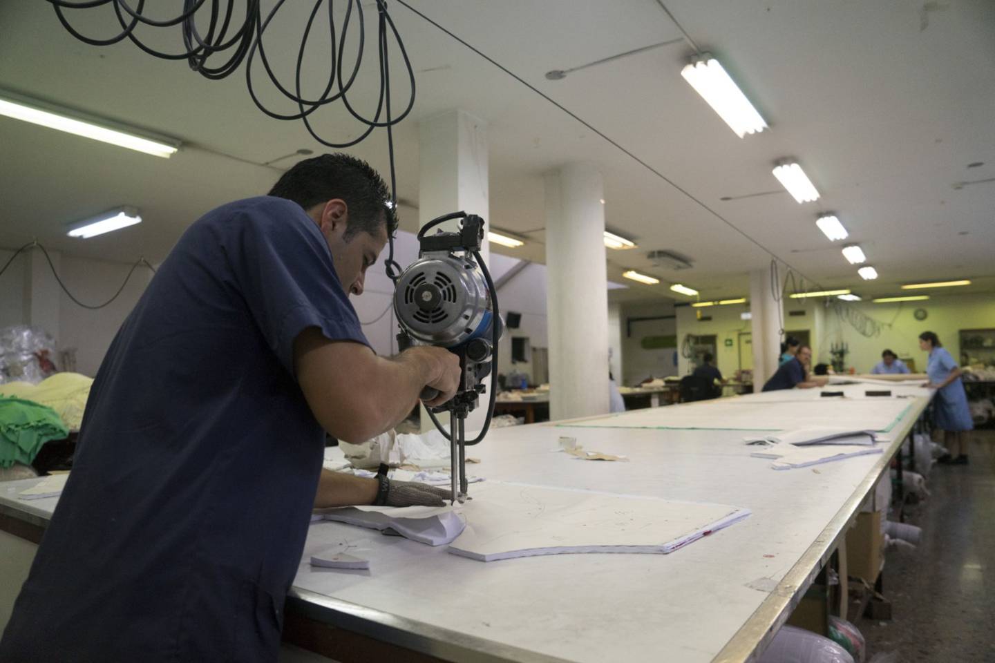 Un trabajador corta una pieza de tela en una fábrica.
