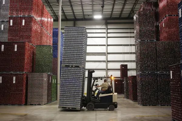 Un trabajador mueve latas de aluminio dentro de un almacén