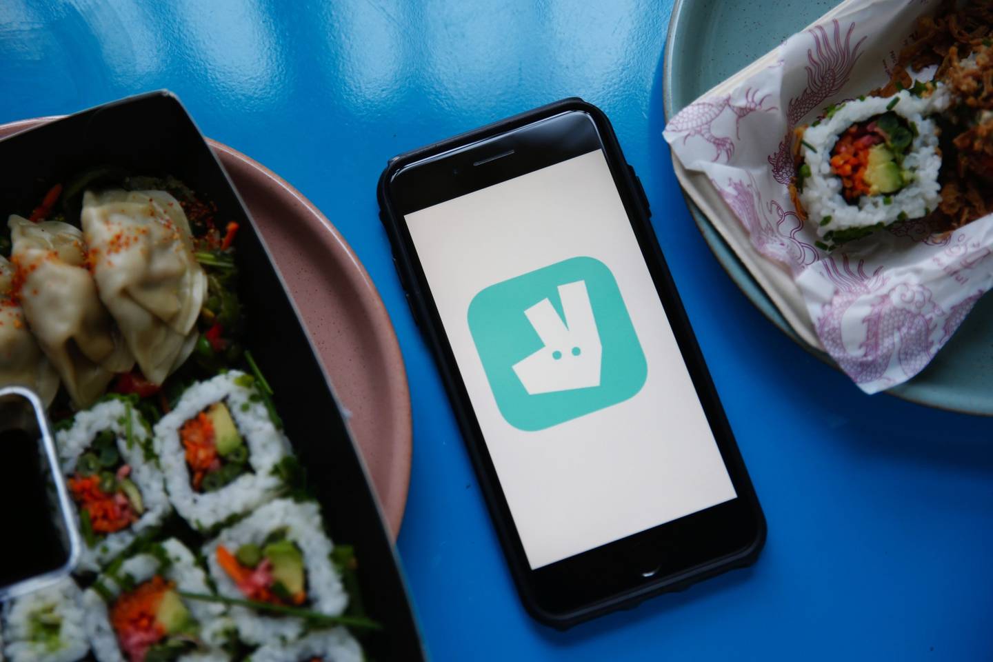 El logotipo de Deliveroo se muestra en un smartphone entre platos de sushi entregados en esta fotografía arreglada en Londres, Reino Unido, el martes 11 de agosto de 2020.