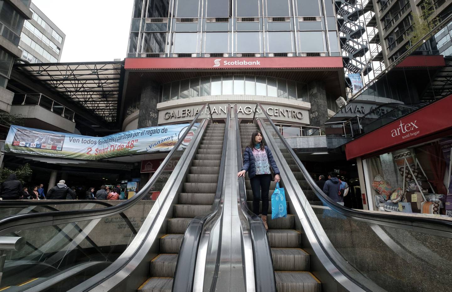 La señalización de Bank of Nova Scotia (Scotiabank) se muestra mientras un comprador sube a una escalera mecánica fuera de la Galería Santiago Chile en Santiago, Chile, el sábado 15 de octubre de 2016.