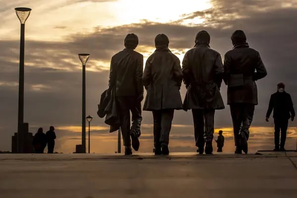 Pedestrians walk past a statue of The Beatles at sunset on Pier Head.