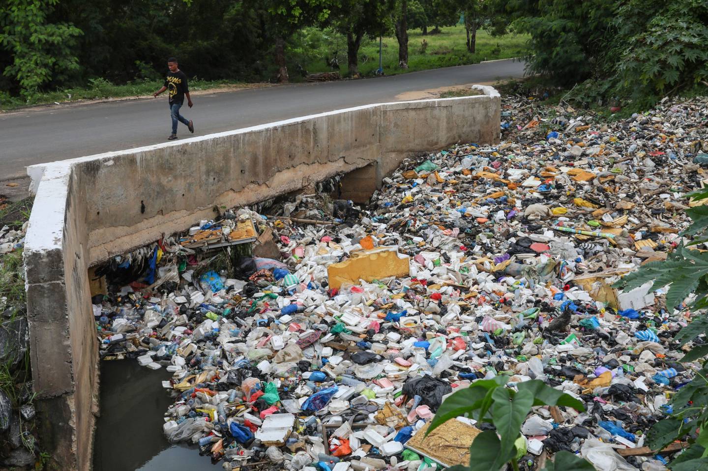 Un peatón camina por un puente sobre una alcantarilla, bloqueada por residuos de plástico y basura, en Accra, Ghana, el lunes 4 de julio de 2022.