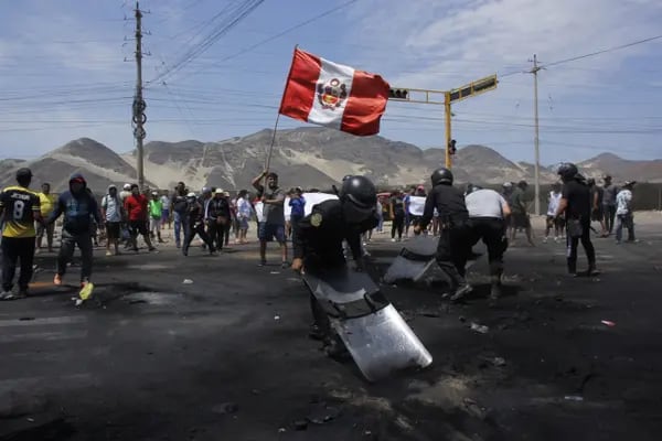 Agentes de la policía antidisturbios barren los escombros mientras un manifestante agita una bandera nacional peruana en la carretera Panamericana Norte durante las protestas en Trujillo, Perú, el jueves 15 de diciembre de 2022. Perú ha declarado el estado de emergencia en todo el país, suspendiendo los derechos básicos durante 30 días, para tratar de restablecer el orden en medio de disturbios violentos generalizados. Fotógrafo: Arturo Gutarra Chavez/Bloomberg