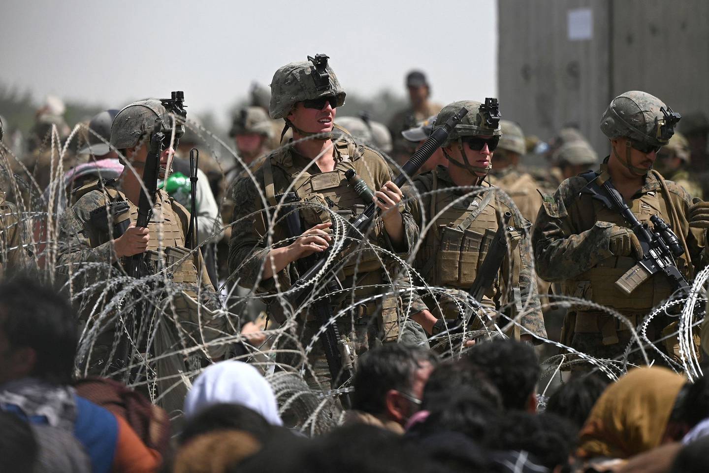 U.S. soldiers stand guard behind barbed wire as Afghans sit on a roadside near the military part of the airport in Kabul on Aug. 20.
