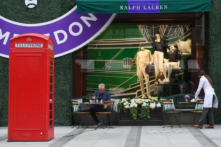 A waitress clears a table outside the Ralph Lauren Corp. store decorated to promote the Wimbledon Tennis Championships, in London, U.K., on Wednesday, June 30, 2021. British households saved a fifth of their disposable income in the first quarter as the U.K. returned to lockdown, adding to a cash pile that is now powering a consumer boom. Photographer: Chris J. Ratcliffe/Bloombergdfd