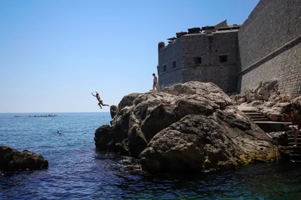 Visitantes haciendo rock-jumping ante las murallas medievales del casco antiguo de Dubrovnik.