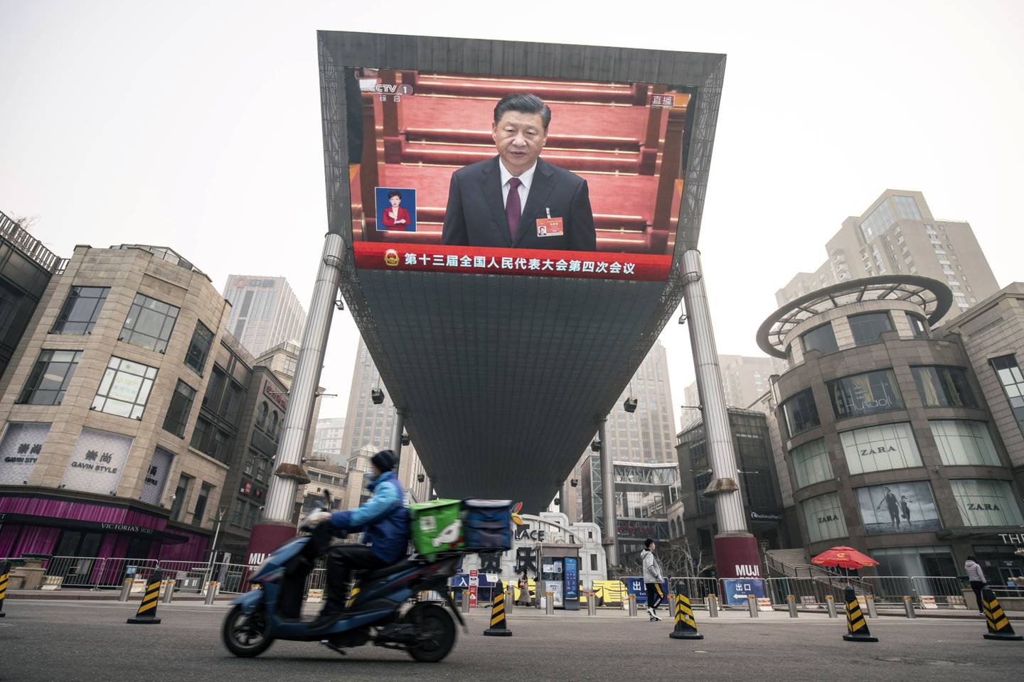 Un repartidor conduce una motocicleta frente a una pantalla que muestra una transmisión de noticias en vivo del presidente chino Xi Jinping en la Asamblea Popular Nacional en Beijing, China. Fotógrafo: Qilai Shen/Bloomberg