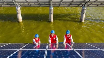 Trabajadores eléctricos revisando los paneles solares de una central fotovoltaica construida en un estanque de peces en Haian, en la provincia china de Jiangsu.  Fotógrafo: STR/AFP/Getty Images