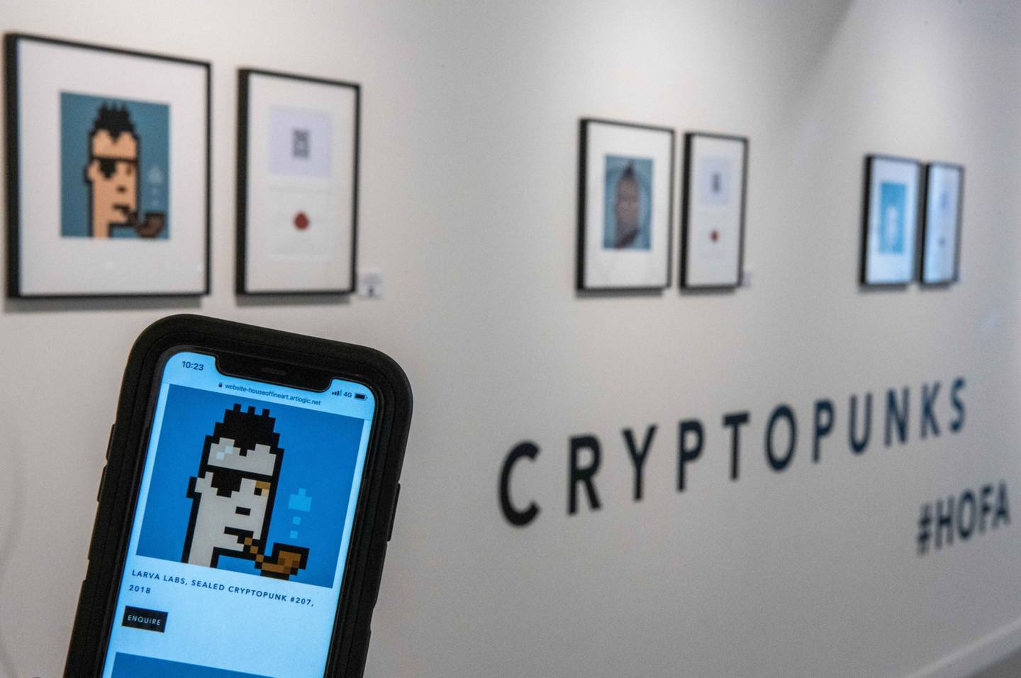 Un asistente de la galería sostiene un teléfono inteligente que muestra la litografía firmada "Sealed Cryptopunk # 207" de Larva Labs.