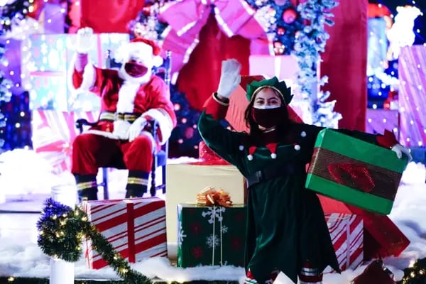 Performers dressed as Santa Claus and an elf wear protective masks while waving during the Night of Lights OC drive-thru Christmas light show at the OC Fair & Event Center in Costa Mesa, California, U.S., on Saturday, Dec. 12, 2020. California's average rate of positive tests over 14 days reached 8.8%, the highest since the spring as cases surged to another record. Photographer: Bing Guan/Bloomberg