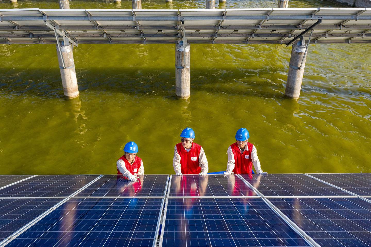 Trabajadores eléctricos revisando los paneles solares de una central fotovoltaica construida en un estanque de peces en Haian, en la provincia china de Jiangsu.  Fotógrafo: STR/AFP/Getty Imagesdfd
