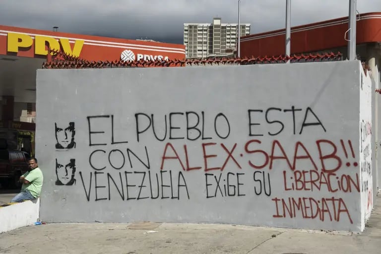 Una persona sentada junto a una pared con un grafiti que dice: "¡El pueblo está con Alex Saab! Venezuela exige su liberación inmediata", en Caracas, Venezuela, el jueves 4 de febrero de 2021. dfd