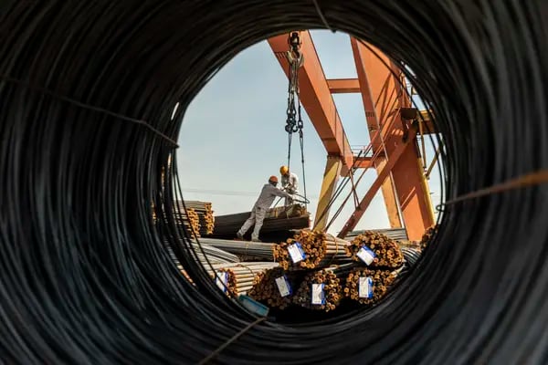 Los trabajadores guían el cable de una grúa de pórtico para levantar un haz de barras de refuerzo de acero en un almacén de metal en Shanghai, China, el lunes 07 de junio 2021.