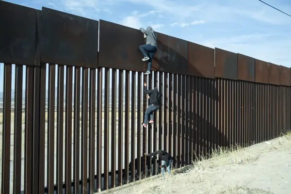 Migrantes intentan escalar el muro en la frontera entre México y Estados Unidos.