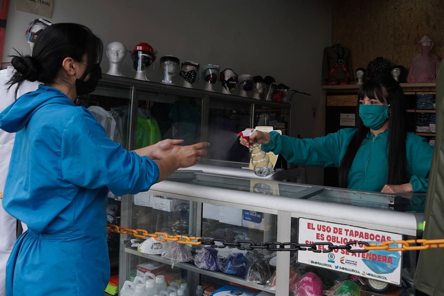 Un trabajador con una máscara protectora rocía desinfectante en las manos de un cliente en Bogotá, Colombia, el martes 16 de junio de 2020.