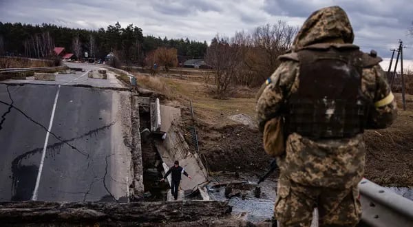 Un soldado ucraniano mira como un civil cruza un puente destruido