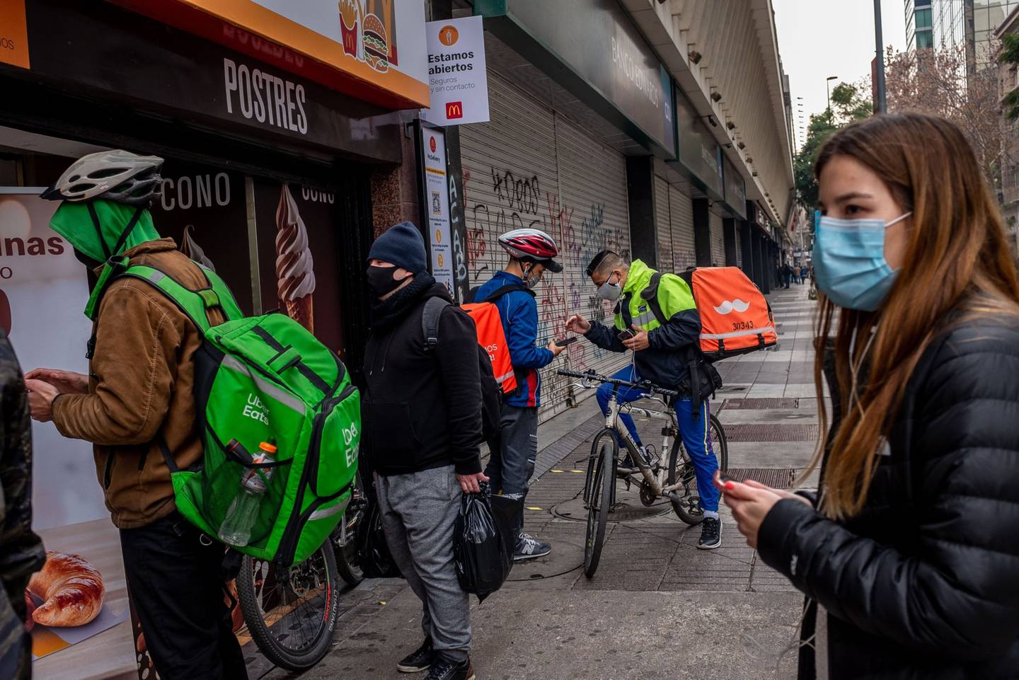 Delivery workers wait outside to pick up food orders in Santiago, Chile, on Monday, July 27, 2020. President Sebastian Pinera signed a bill into law late Friday allowing Chileans to withdraw retirement savings, following scenes of citizens lining up by the thousands outside pension fund offices. Photographer: Cristobal Olivares/Bloomberg