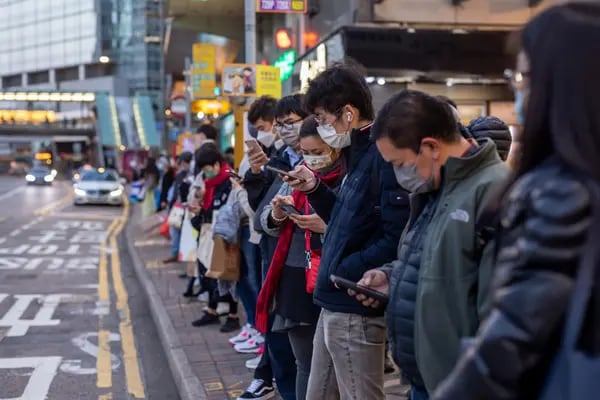Los viajeros miran sus teléfonos inteligentes mientras están en una parada de autobús en Hong Kong, China, el viernes 4 de febrero de 2022.