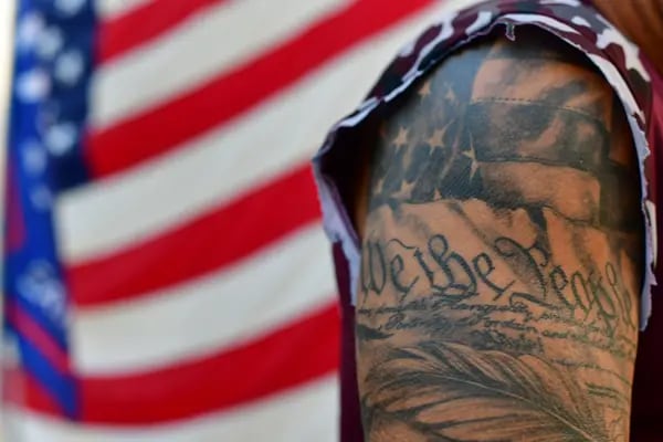 Un tatuaje dice "We the People" (Nosotros, el pueblo), mientras Chris Cox, de 51 años, sujeta postes de la bandera de Estados Unidos a una barricada mientras se manifiesta fuera del lugar donde todavía se están contando los votos en Pensilvania, siete días después de las elecciones generales el 10 de noviembre de 2020 en Filadelfia, Pensilvania.