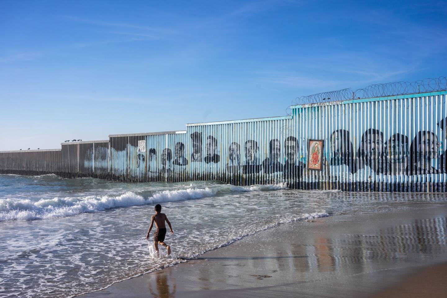 Un niño juega en el agua de una playa cercana a un tramo de la valla fronteriza entre México y Estados Unidos en Tijuana.