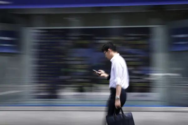 Peatón pasa frente a una pizarra electrónica con información sobre la Bolsa de Tokio