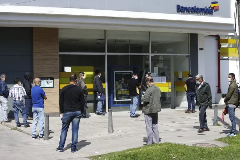 Hombres con máscaras protectoras hacen fila, mientras practican el distanciamiento social, frente a un banco en Bogotá, Colombia, el lunes 13 de abril de 2020.dfd