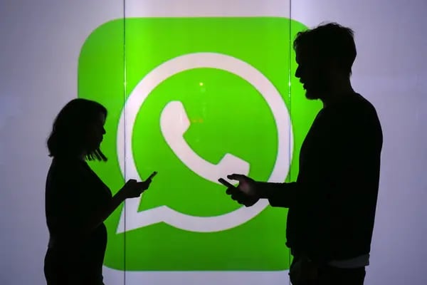 Personas que miran sus dispositivos móviles frente a una pared iluminada con el logotipo de WhatsApp Inc.