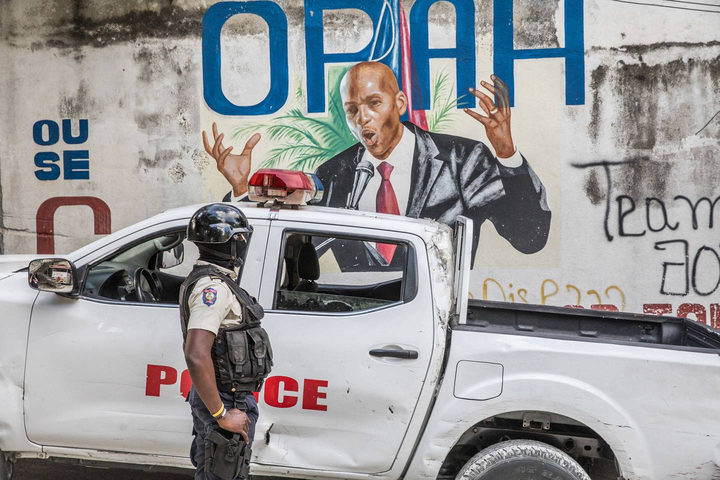 Un oficial de policía se encuentra junto a una pared pintada con un mural del fallecido presidente haitiano Jovenel Moise después de que agentes del FBI y equipos forenses realizaron búsquedas en su residencia en Puerto Príncipe el 15 de julio de 2021.