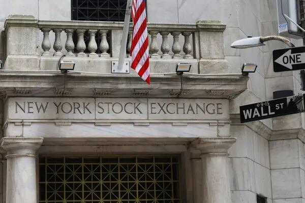 Parte da fachada da Bolsa de Valores de Nova York, com foco no letreiro "New York Stock Exchange". Na parte direita da imagem é possível ver a placa com o nome da rua – Wall Street.