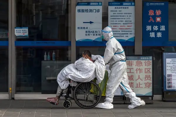 Un trabajador sanitario con equipo de protección empuja a un paciente en una silla de ruedas en un hospital de Pekín, China, el miércoles 14 de diciembre de 2022.