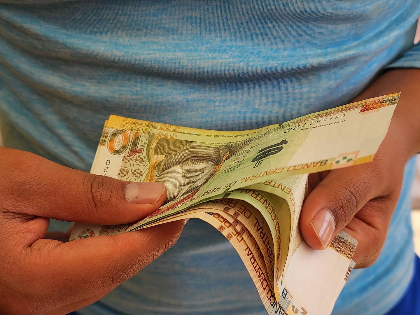 Manos de un hombre sosteniendo y contando billetes peruanos.