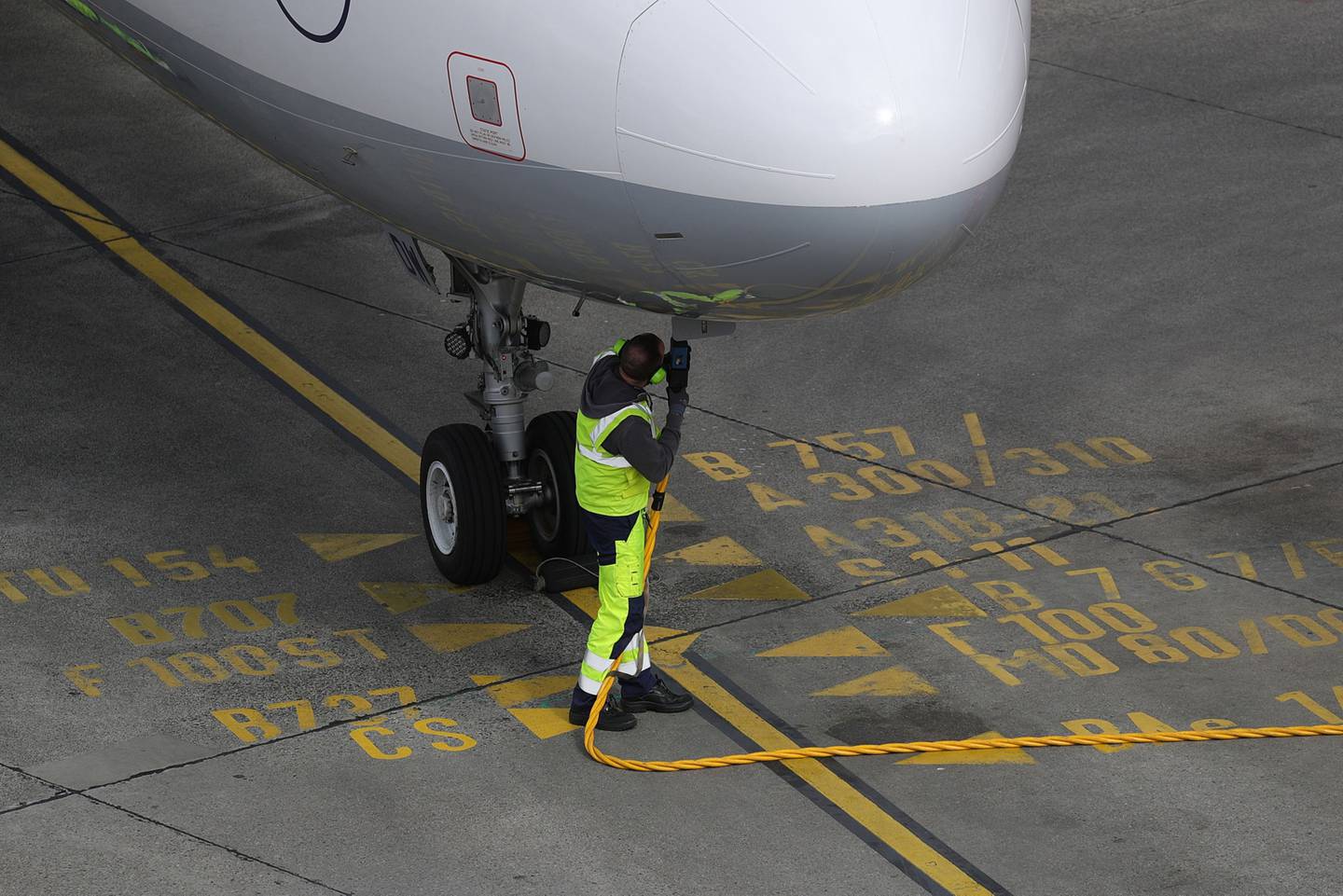 Un trabajador de aeropuerto conecta una manguera de combustible a un avión.