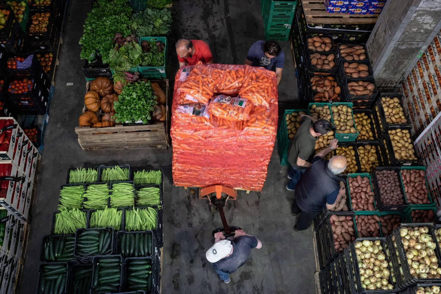 Trabajadores empujan un cargador de palets lleno de sacos de zanahorias dentro de un distribuidor en Oporto, Portugal.