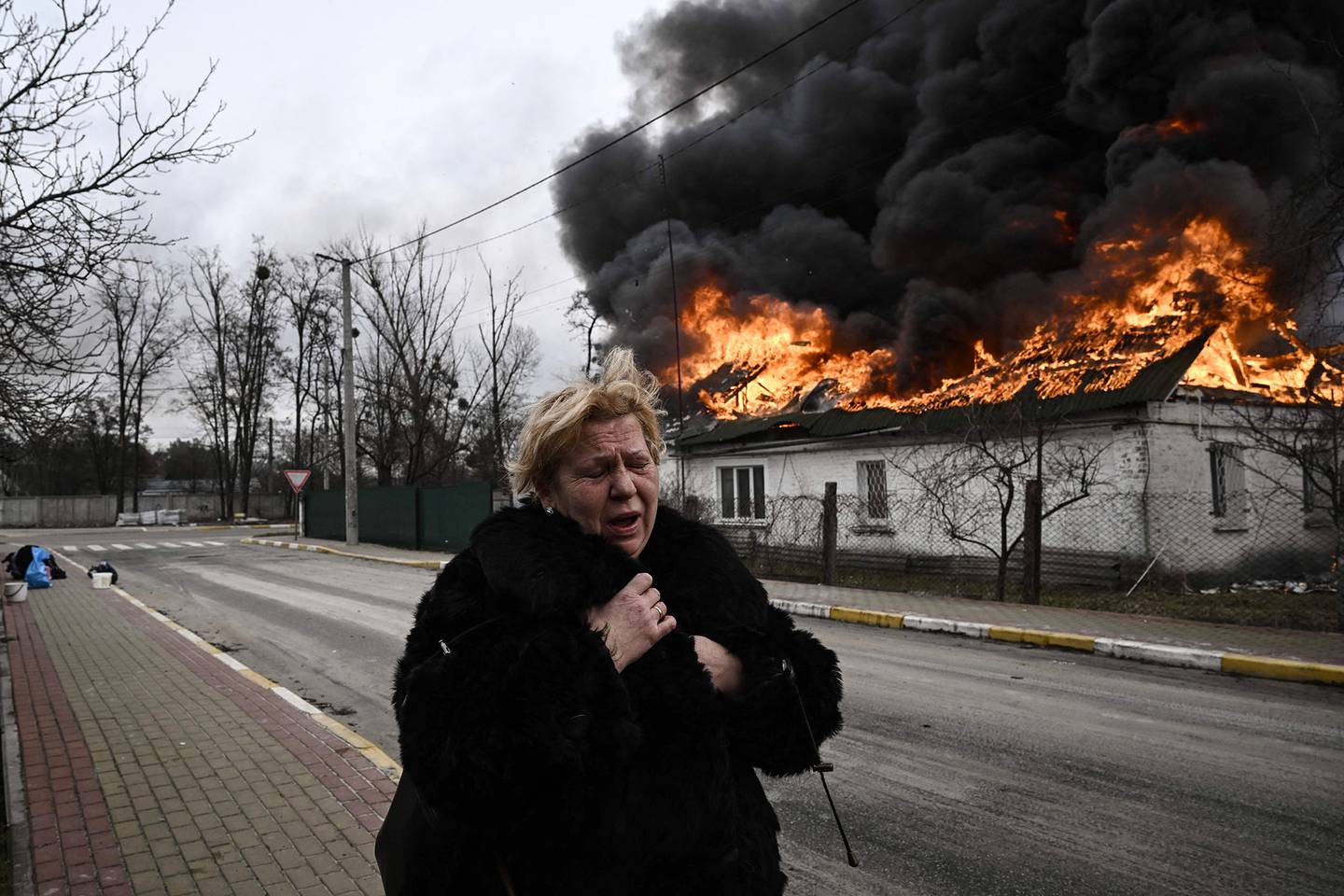 Uma mulher está perto de uma casa em chamas em Irpin, nos arredores de Kiev, em 4 de março.Fotógrafo: Aris Messinins/AFP/Getty Imagesdfd