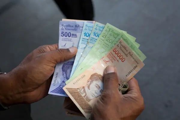 Una persona sostiene un billete de 500.000 bolívares junto a los antiguos billetes de 10.000, 20.000 y 50.000 bolívares frente a un banco en Caracas, Venezuela.