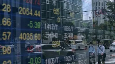 Peatones se reflejan en un tablero electrónico de acciones en el exterior de una empresa de valores en Tokio, Japón.