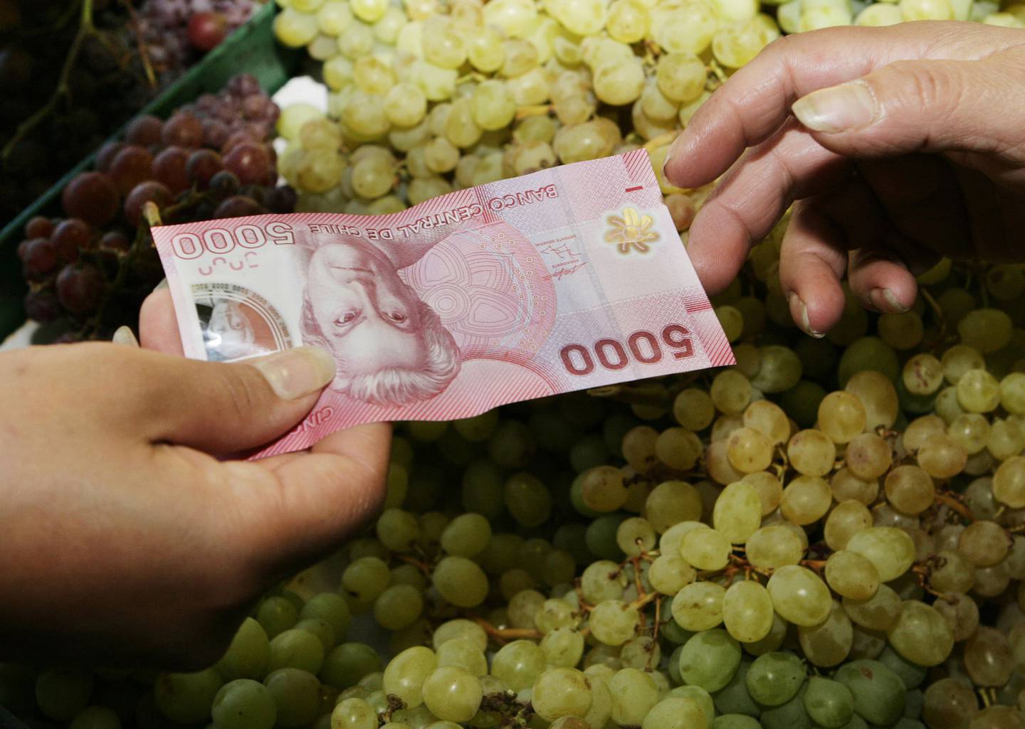 Un cliente paga las compras con un billete de 5000 pesos chilenos en un carrito de frutas en Santiago, Chile.